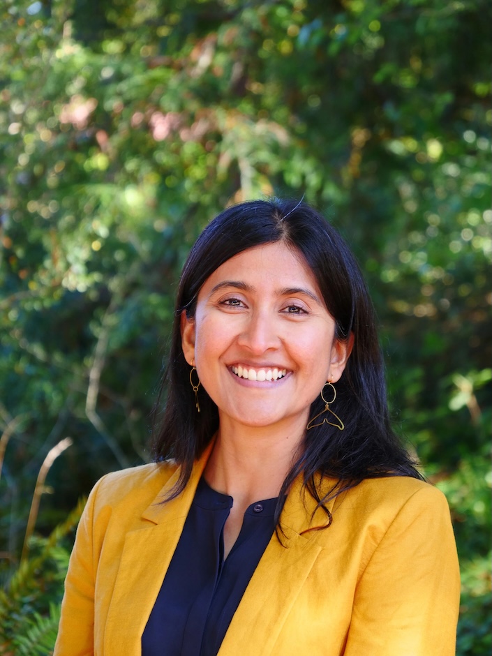 Headshot of Deepti Chatti in yellow jacket with green, nature background