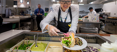 A woman holds a plate with a plant-forward meal in a UC San Diego kitchen.