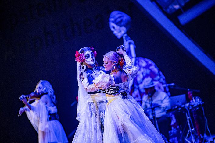 A woman with her face painted like a skeleton dances with a vocalist from Las Cafeteras, both dressed in white lace skirts.
