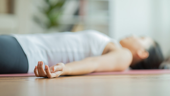 Person lies on back on floor on yoga mat with palms facing up