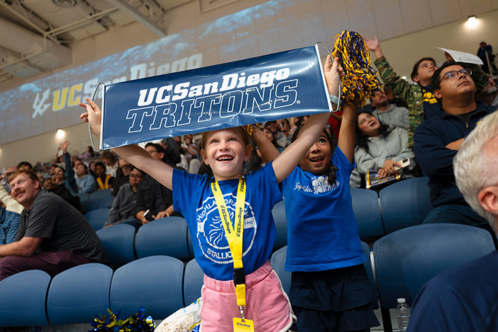 Two children in stands hold up a UC San Diego Tritons sign and a pom pom