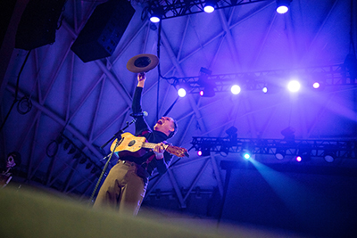 Las Cafeteras band member Hector Flores lifts his hat as he plays guitar and sings.