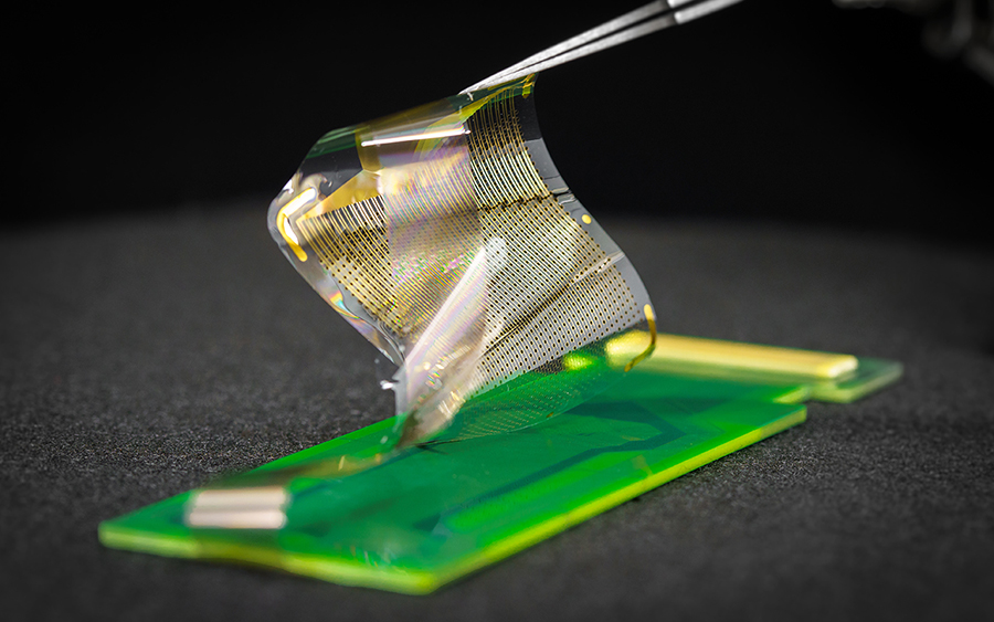 A thin, plastic-like square of electronic sensors is held up by tweezers.