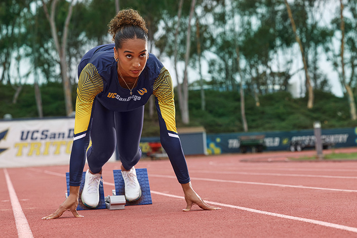 Runner crouches on track with feet on starting blocks.