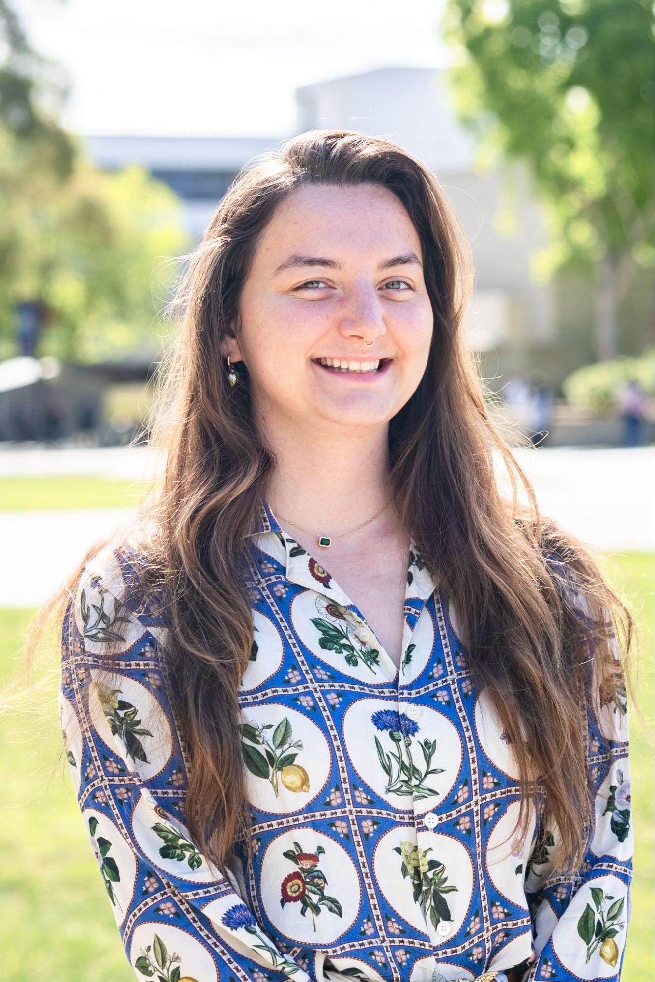 person smiling at the camera wearing a patterned button down shirt