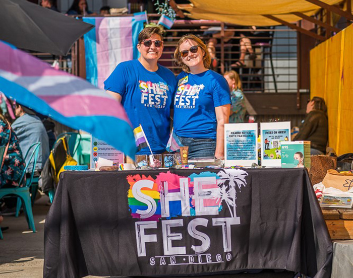 Jeanette and a friend pose in front of a table promoting She Fest