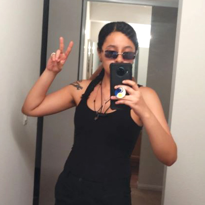 Kiki Drew takes a photo of herself with a phone looking in the mirror holding a peace sign