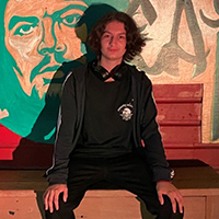 Preuss graduate Liam Rodriguez sitting in front of a mural