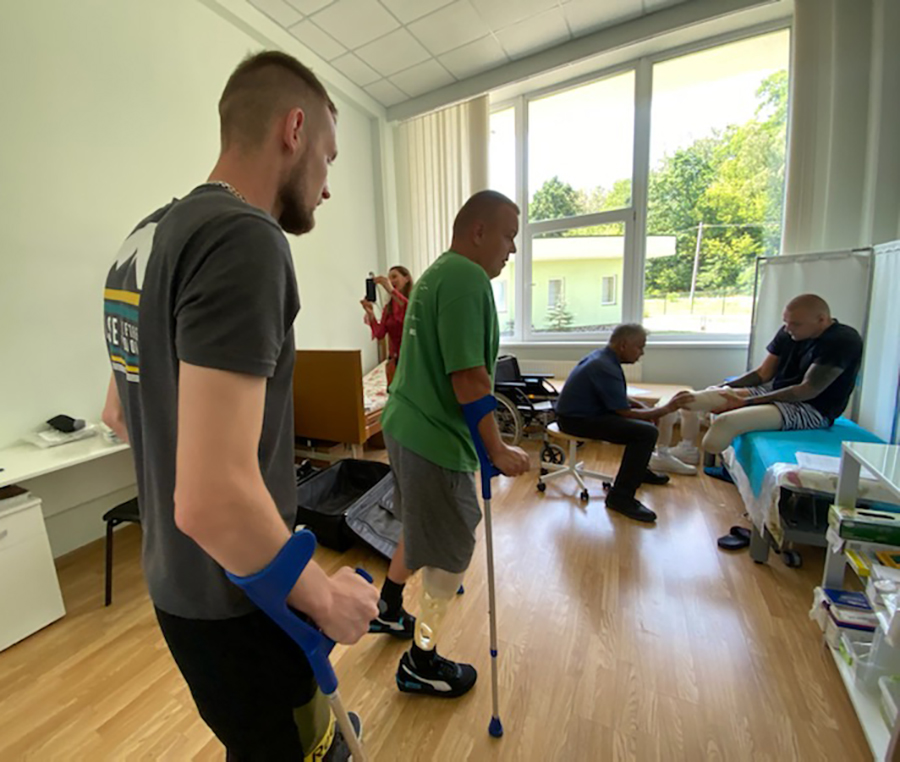 Two patients look on as Dr. Monga fits a prosthetic limb on an amputee.