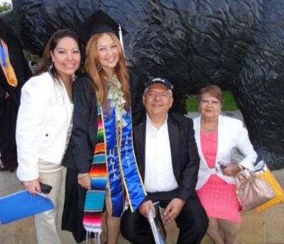 A student in cap and gown with her family after graduation.