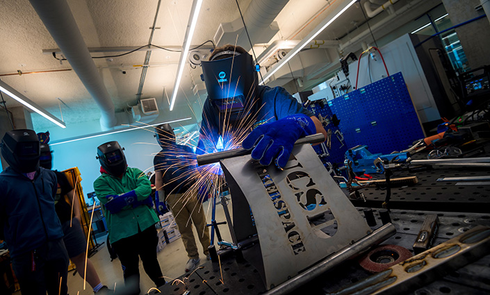 A student welding, with sparks flying, a metal sign that says