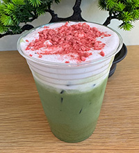 A green match tea drink is topped by a white foam and pink dried fruit pieces.