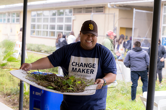 A UC San Diego staff member holds a bucket of plants that were pulled from the ground to clear space for students with wheelchairs to enter the garden.