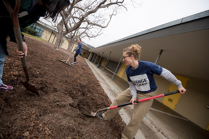 Three students use shovels to move around mulch that surrounds a sensory garden designed for students with disabilities.