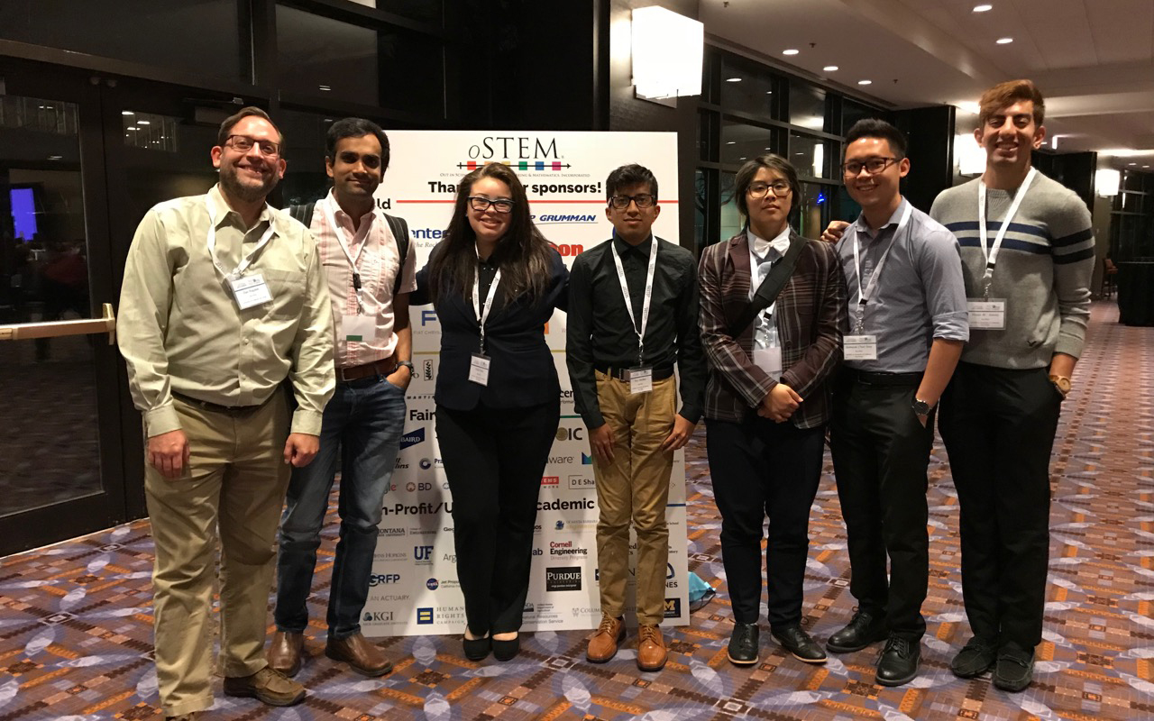 Photo of two professors at left and at right five undergraduate students in front of a sign for oSTEM conference they attended.