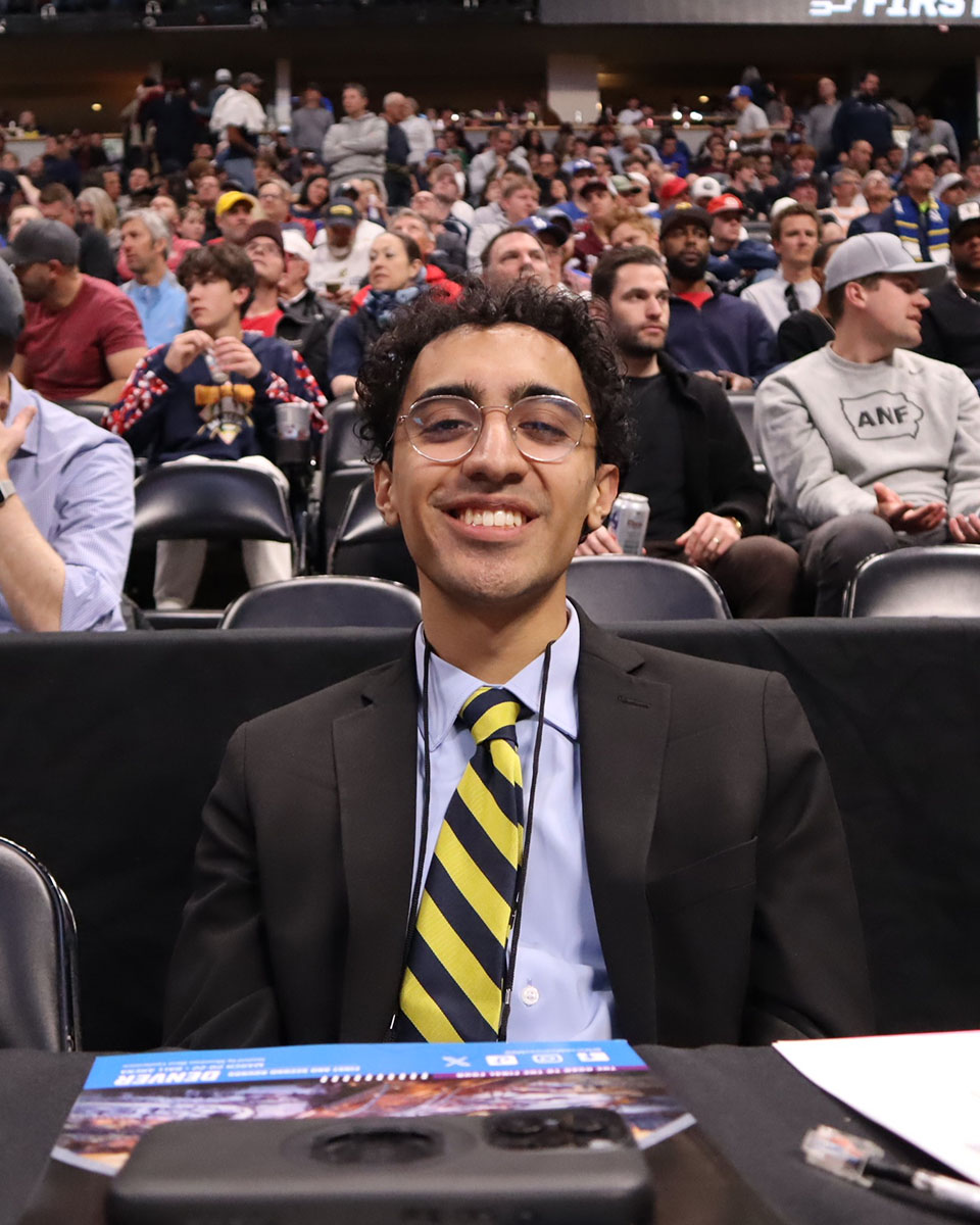 Student in suit smiles at basketball scorers' table
