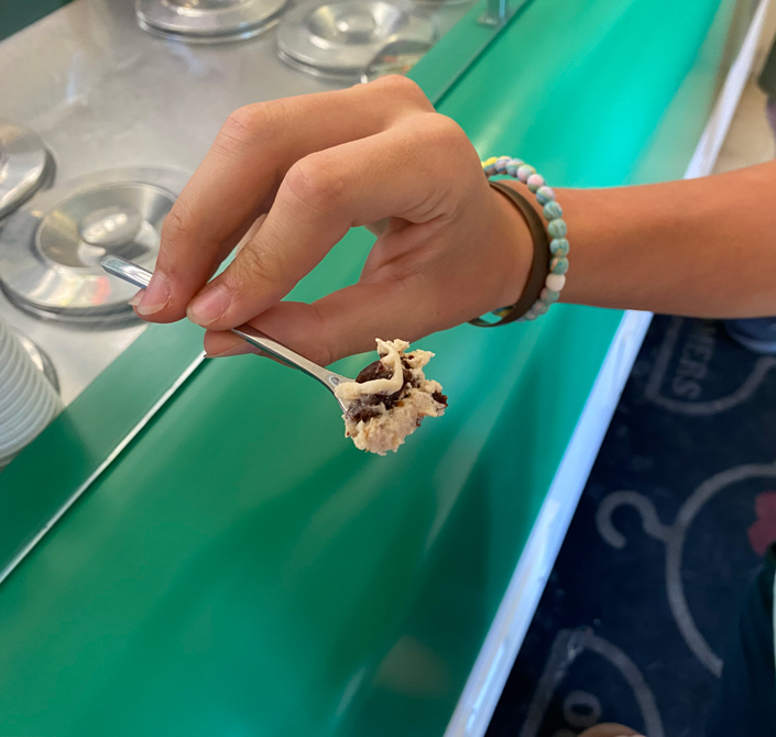 A hand holds a tasting spoon of gelato.