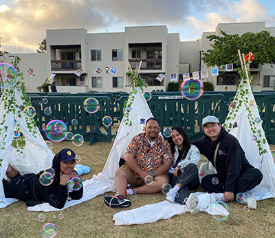 Graduating student Princess Labrador sits on the grass with her three mentors, surrounded by bubbles and miniature tents.