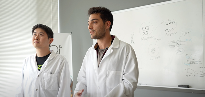 Two men in lab coats in front of whiteboard