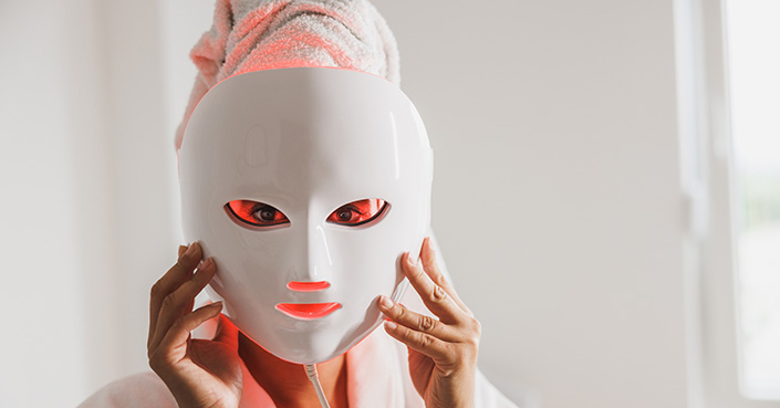 Person holds red light LED mask up to their face