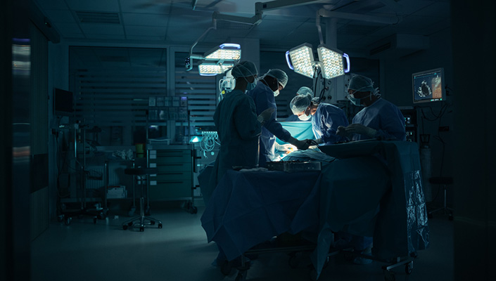 Four medical personnel perform surgery under a light