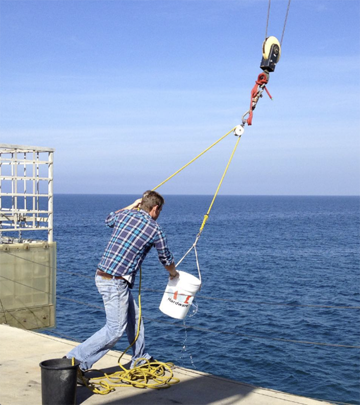 A researcher collects water off a pier using a bucket.