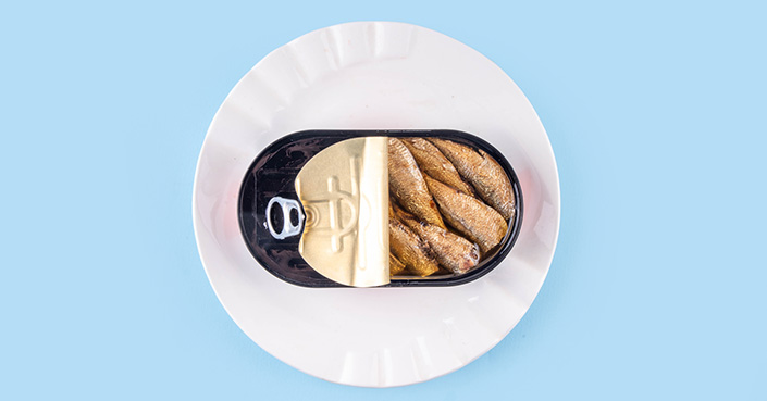 Can of sardines on white plate against blue background