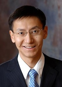 Portrait of a man in a light blue collared shirt against a plain gray background.
