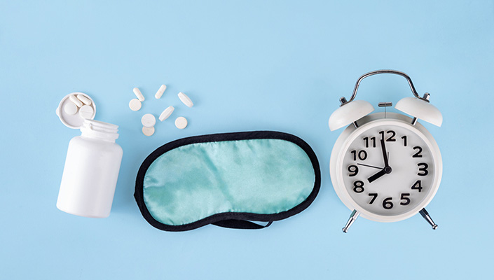 Bottle of supplements, eye mask and alarm clock on a blue background