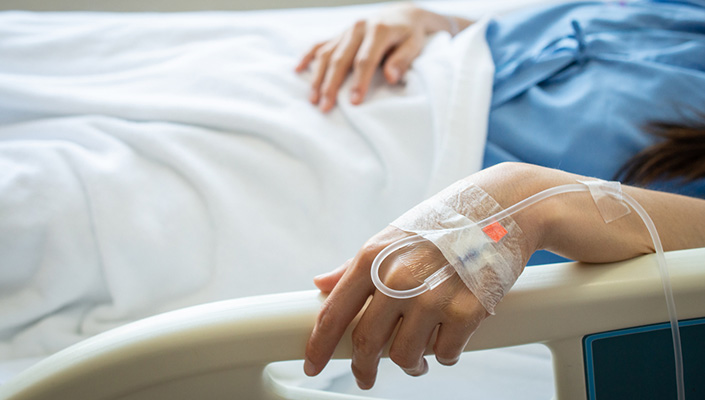 Hand with IV inserted holds on to hospital bed rail