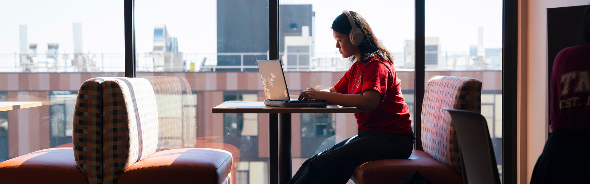 Student sits at laptop in front of a large window.