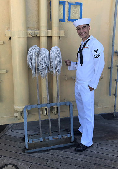 Tom Bowers dressed in sailor outfit on a Navy ship next to mops