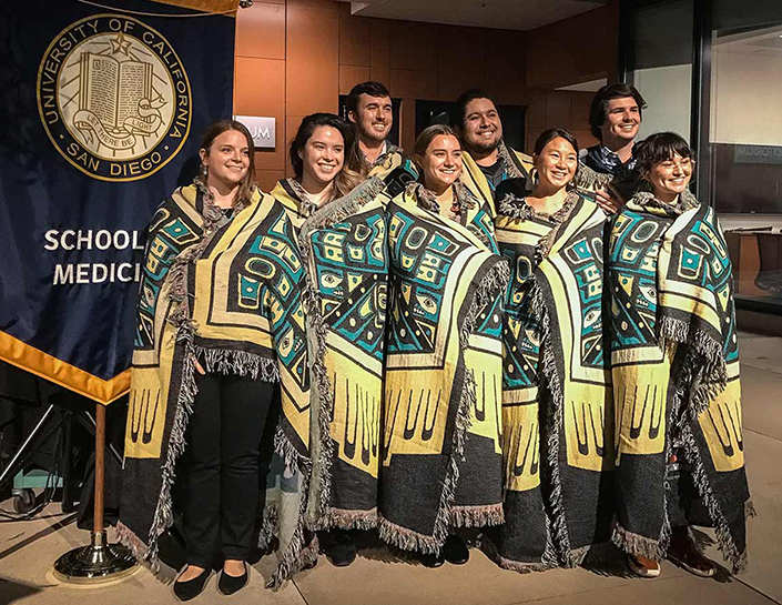 A group of eight students at the UC San Diego School of Medicine pose wrapped in a Native American blanket during the school's first blanketing ceremony in 2021.