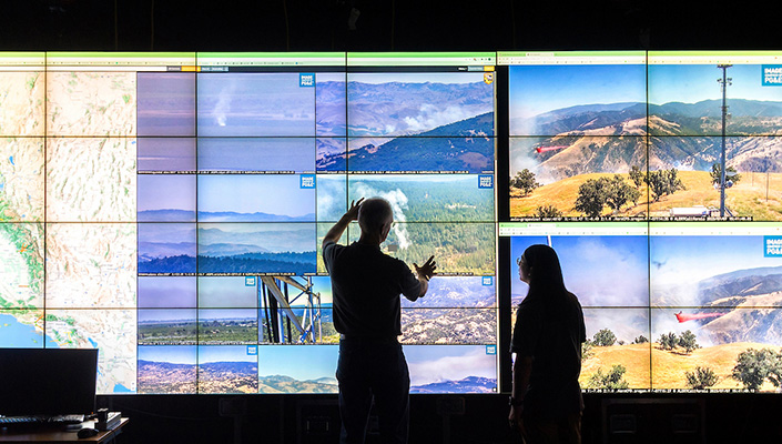 Two individuals look up at camera feeds on large screen