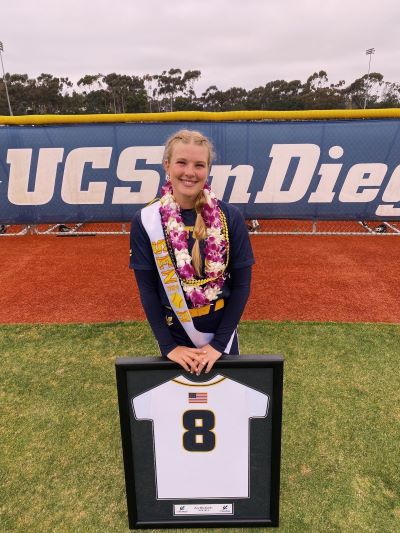 A softball player smiling with her framed team-jersey number before graduating