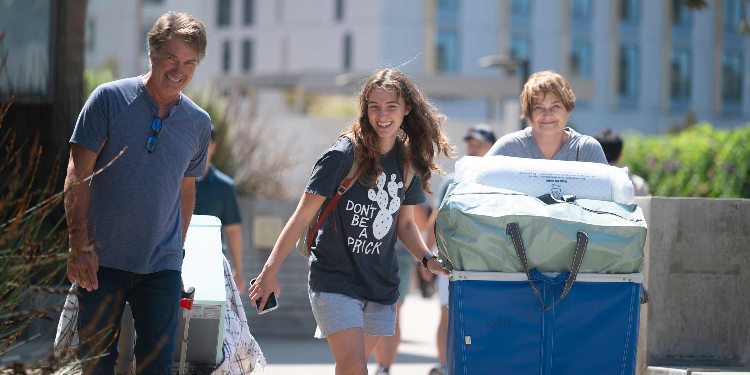 A student and two adults wheel luggage in a cart.
