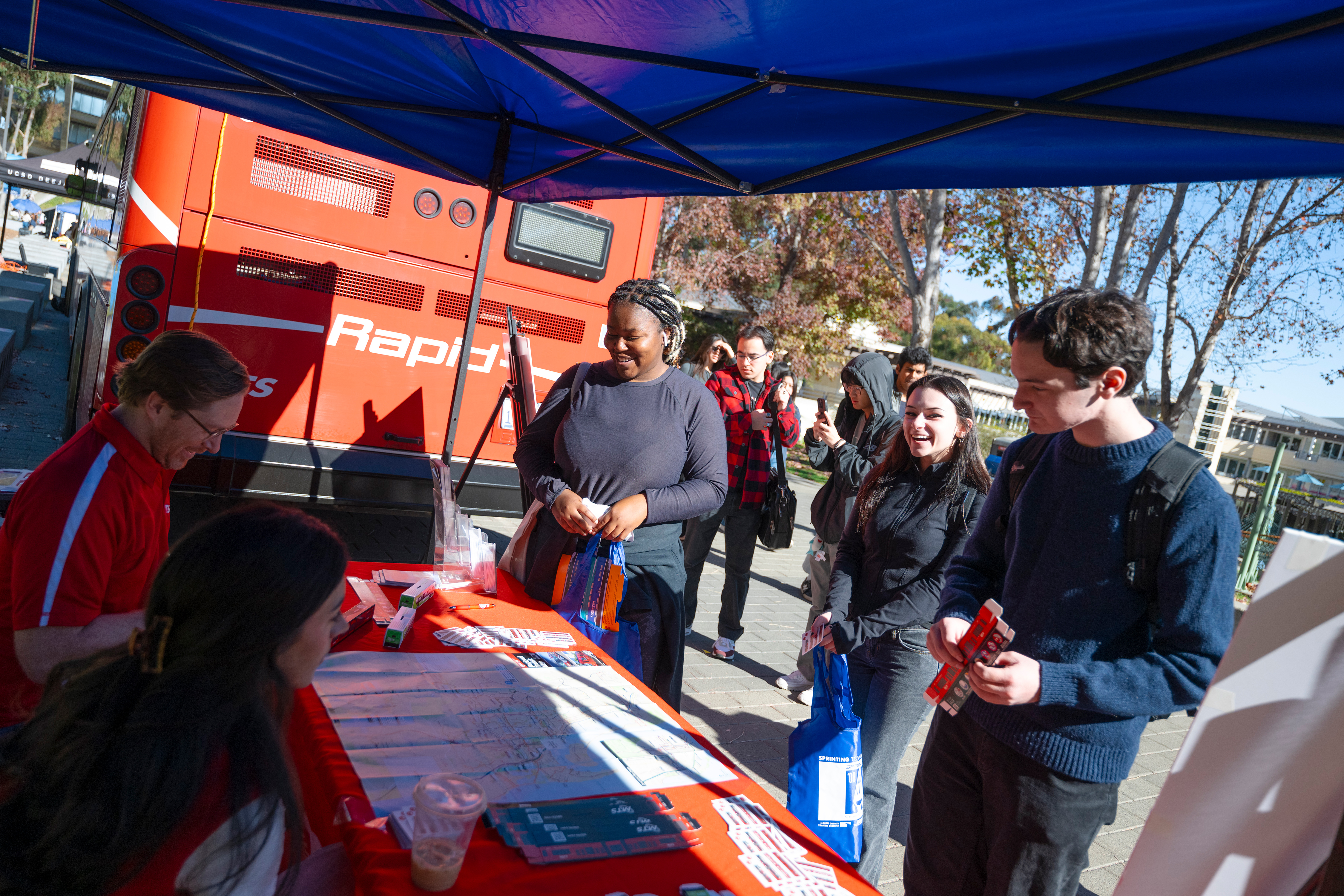 Three people in front of a booth next to a bus chat with two people behind the booth