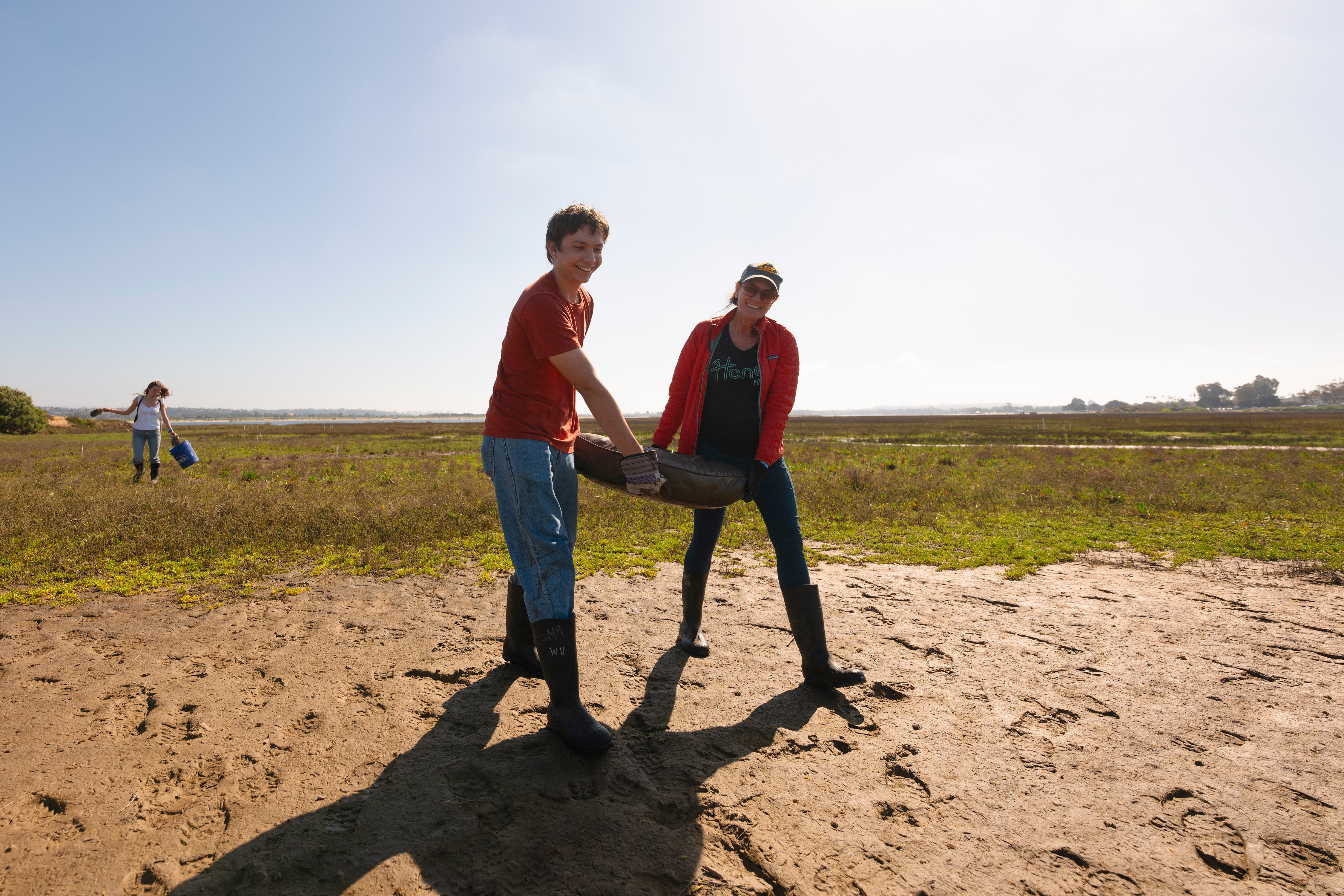 Two people carry a couch cushion.