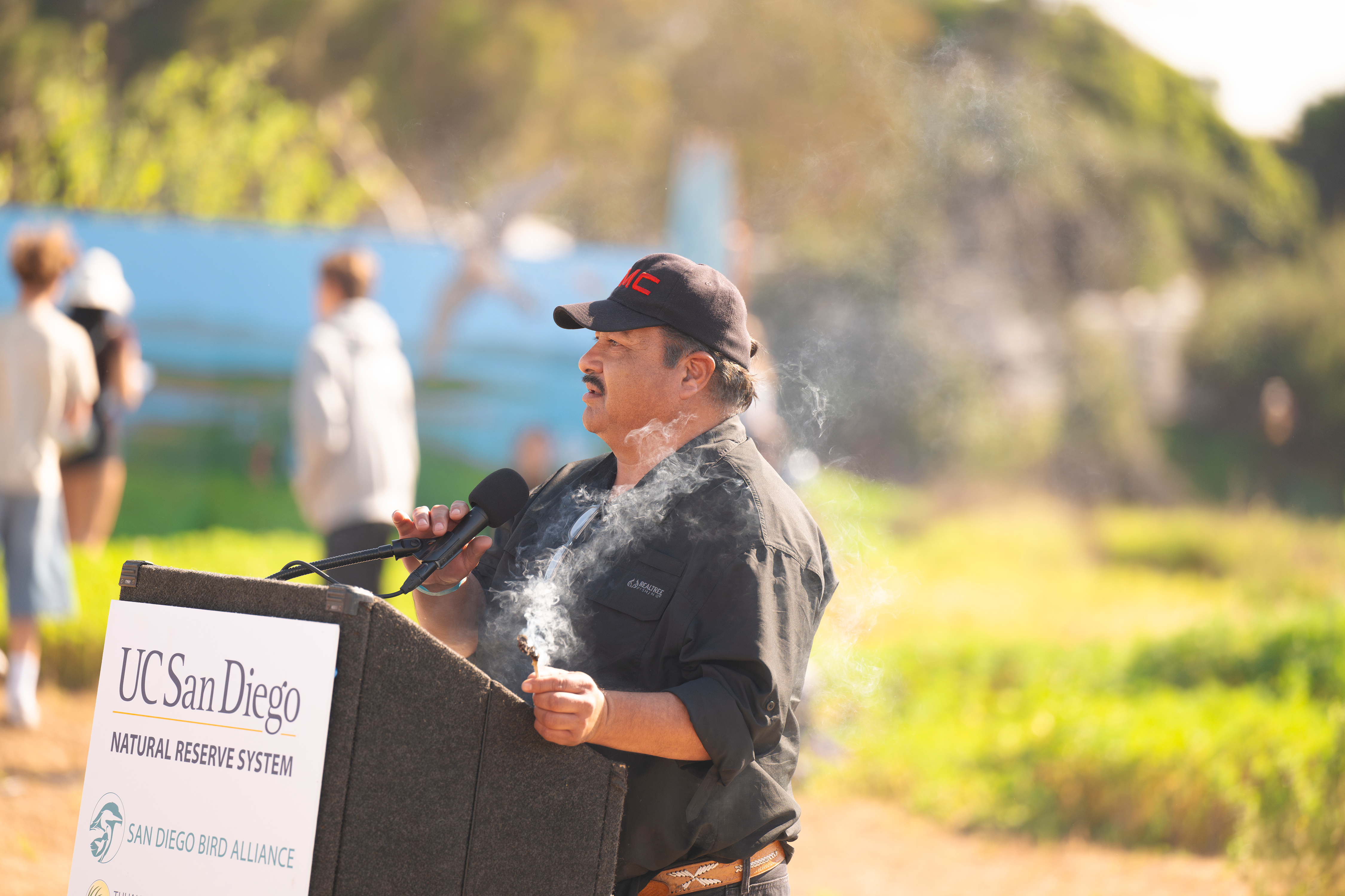 A man stands at the podium with a bundle of smoking herbs.