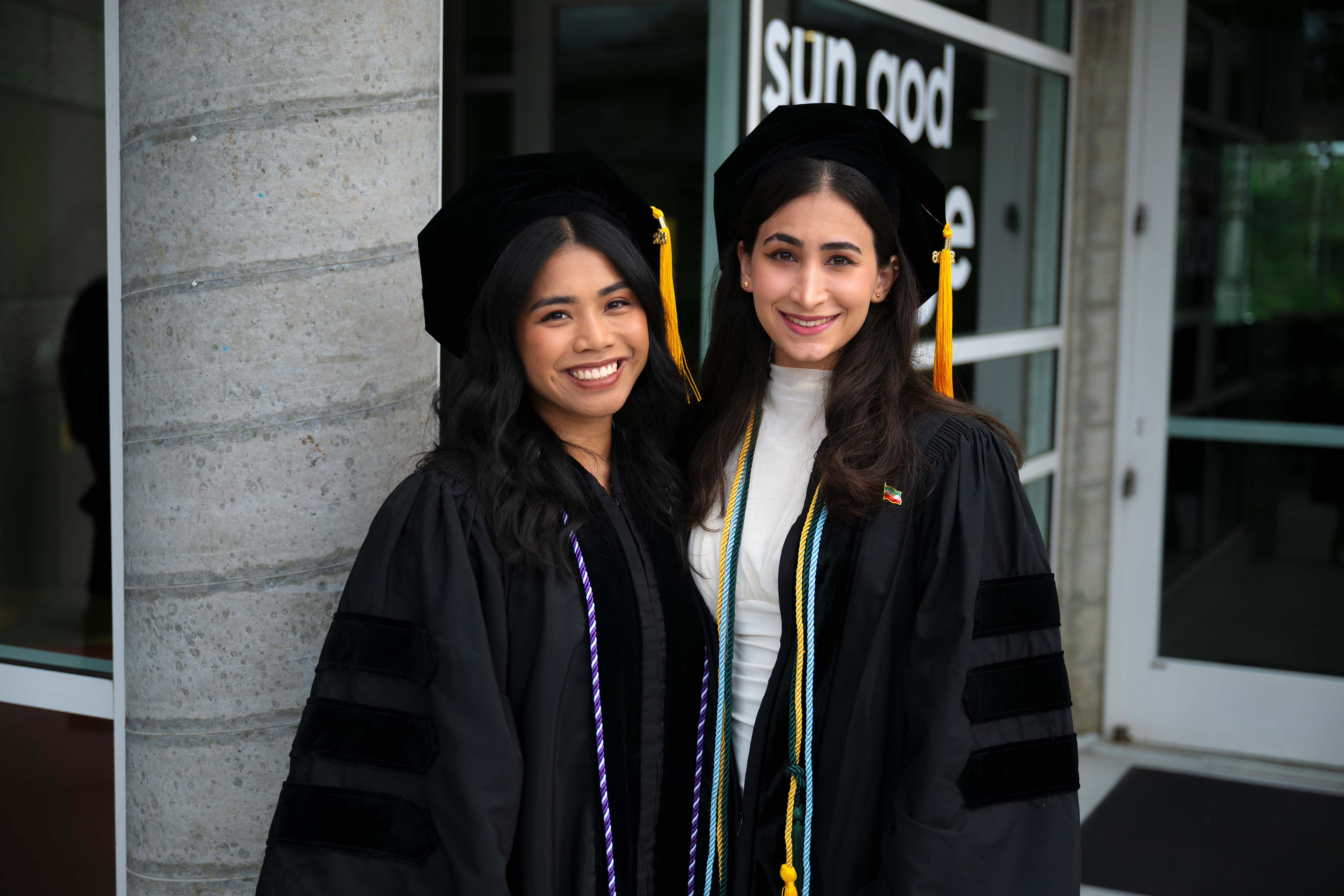Two women in graduation gowns celebrate the Class of  2026 commencement.