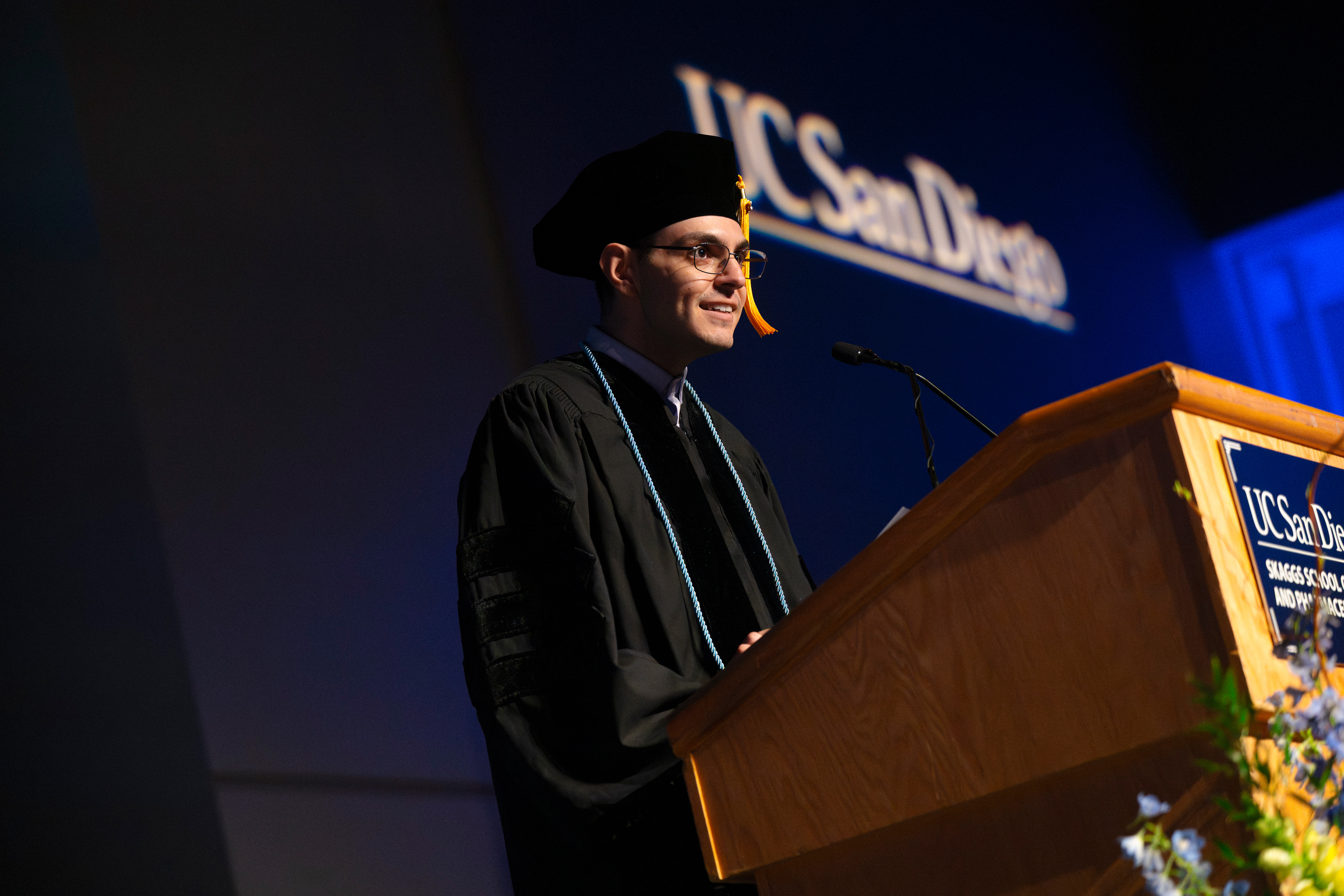 Male student at podium speaks at 2026 Skaggs Commencement ceremony. 