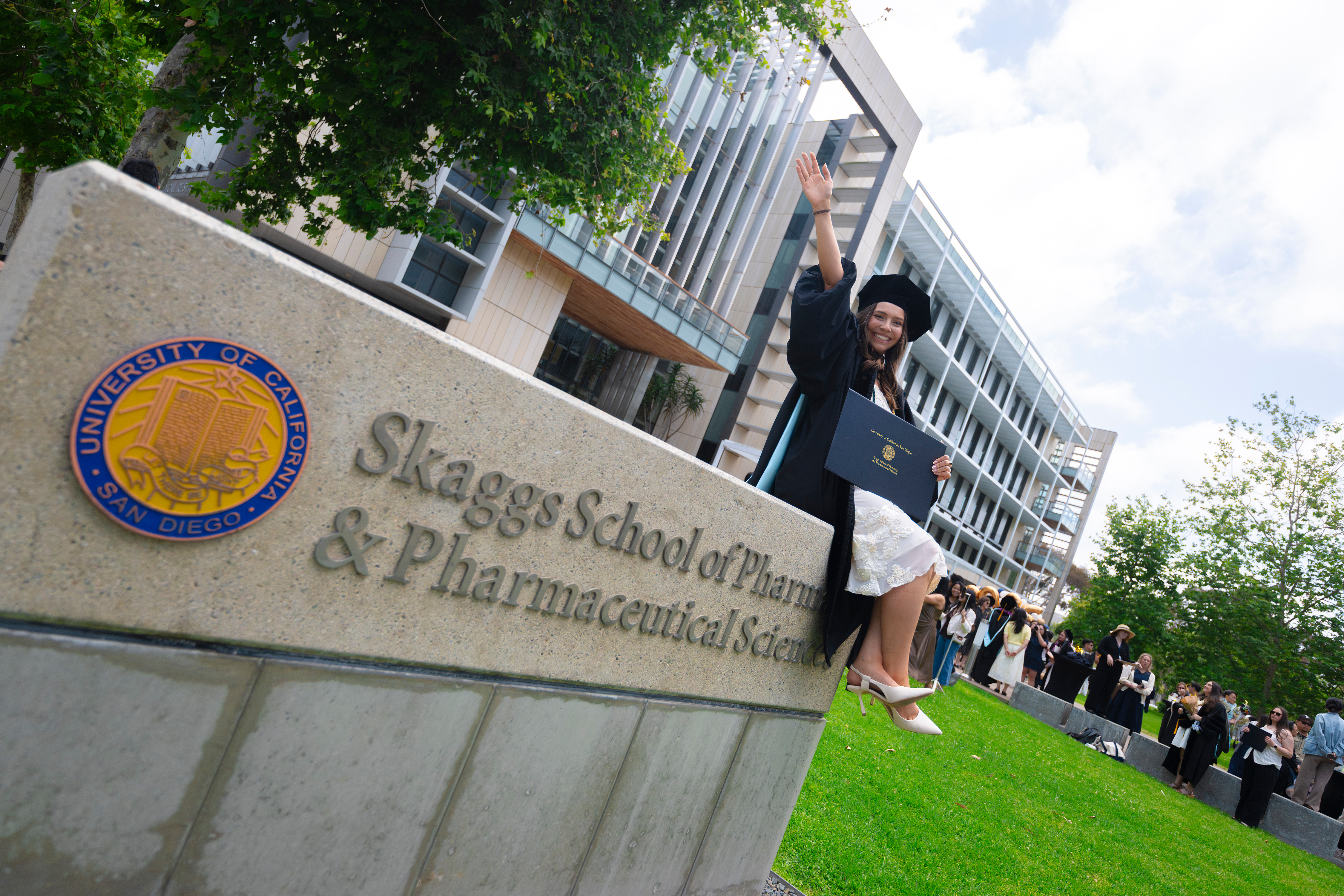 Female student holding her diploma while sitting on the Skaggs Schools of Pharmacy and Pharmaceutical Sciences sign.