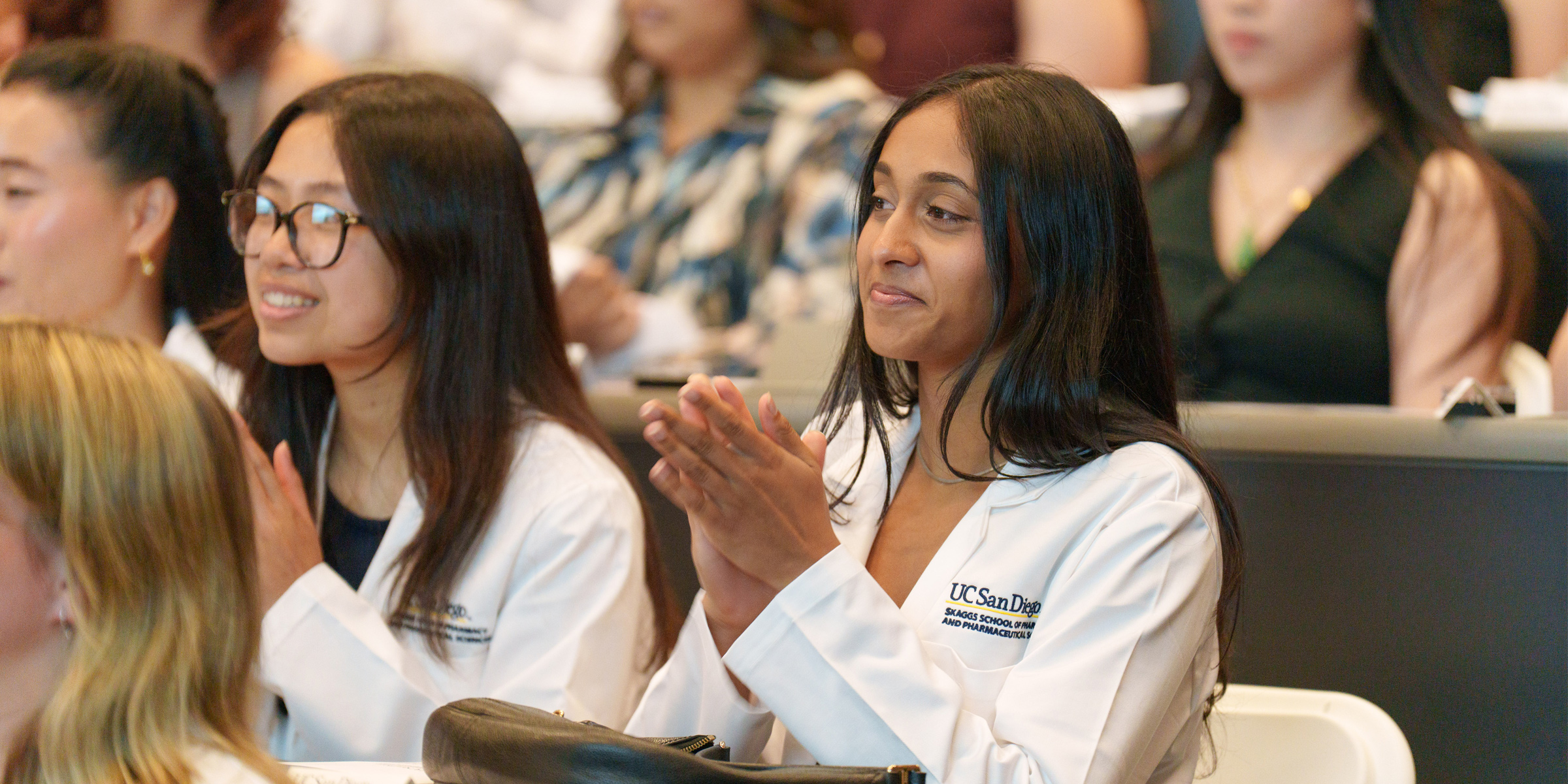 Female sitting down clapping while wearing a white coat.