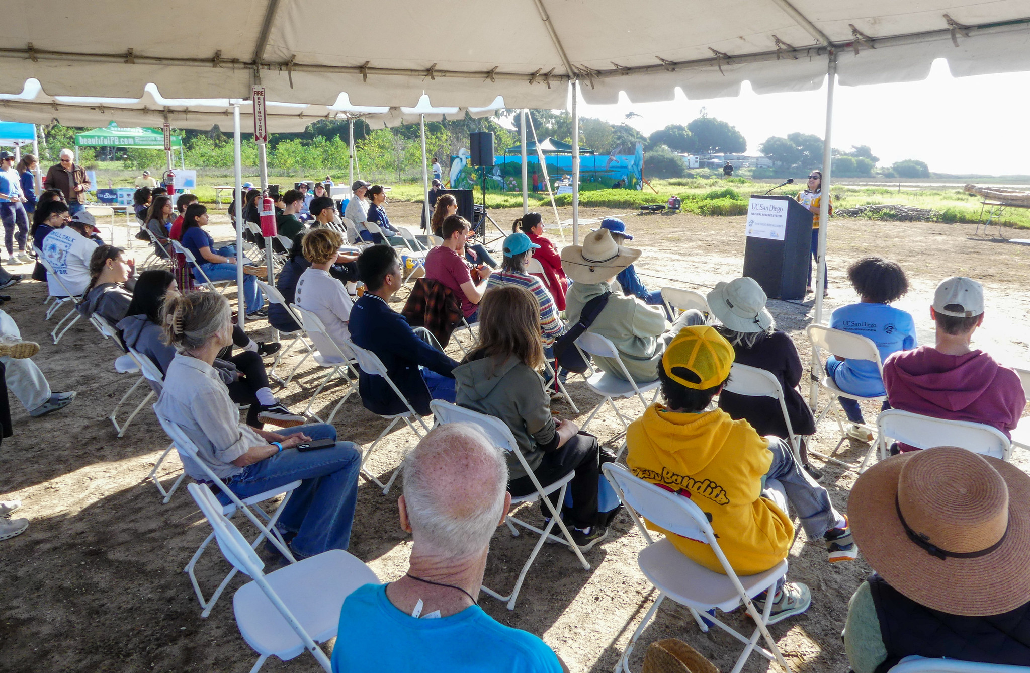 Speaker at podium addresses audience under tent