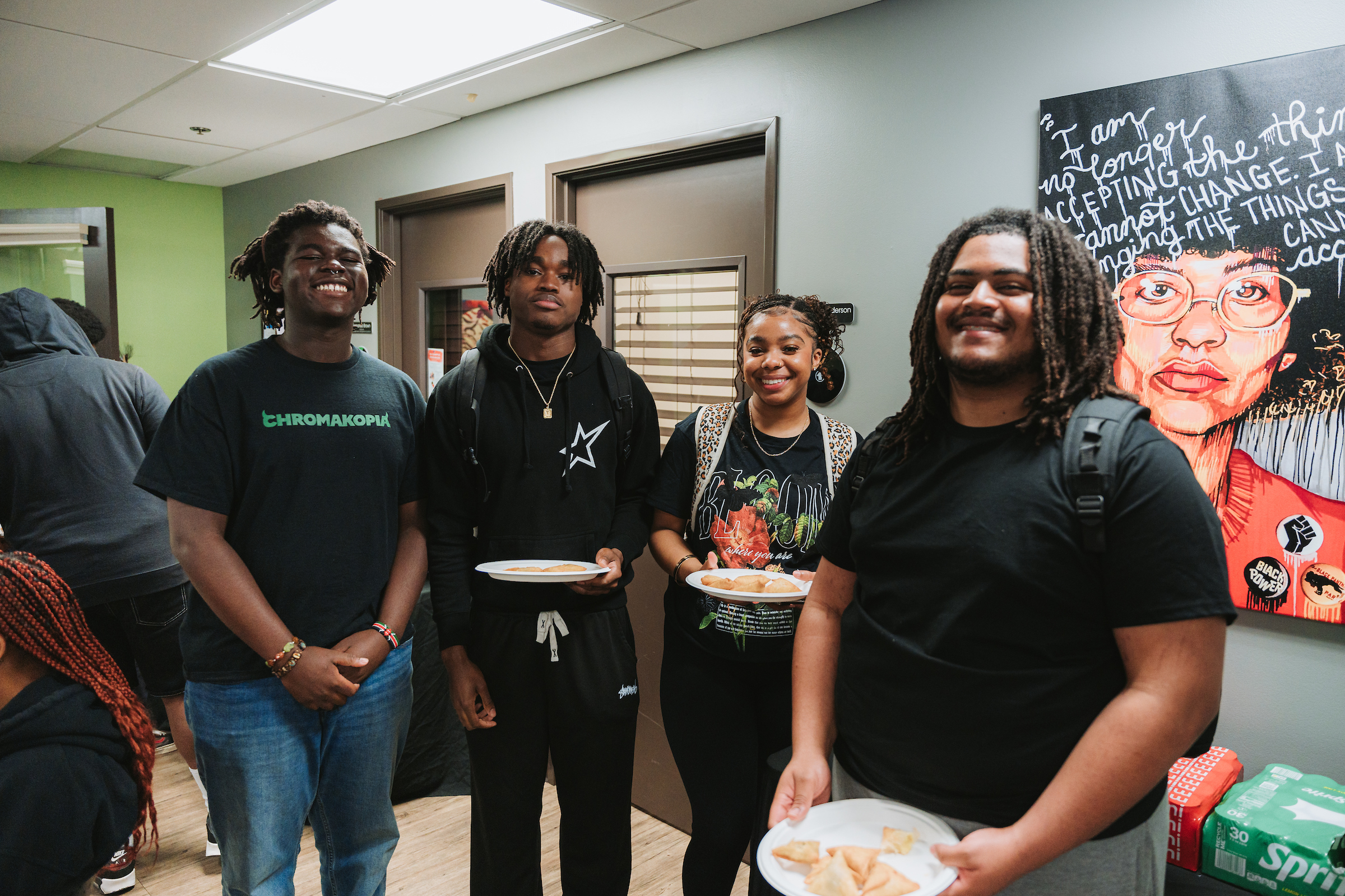 Four people hold plates of food while smiling at the camera
