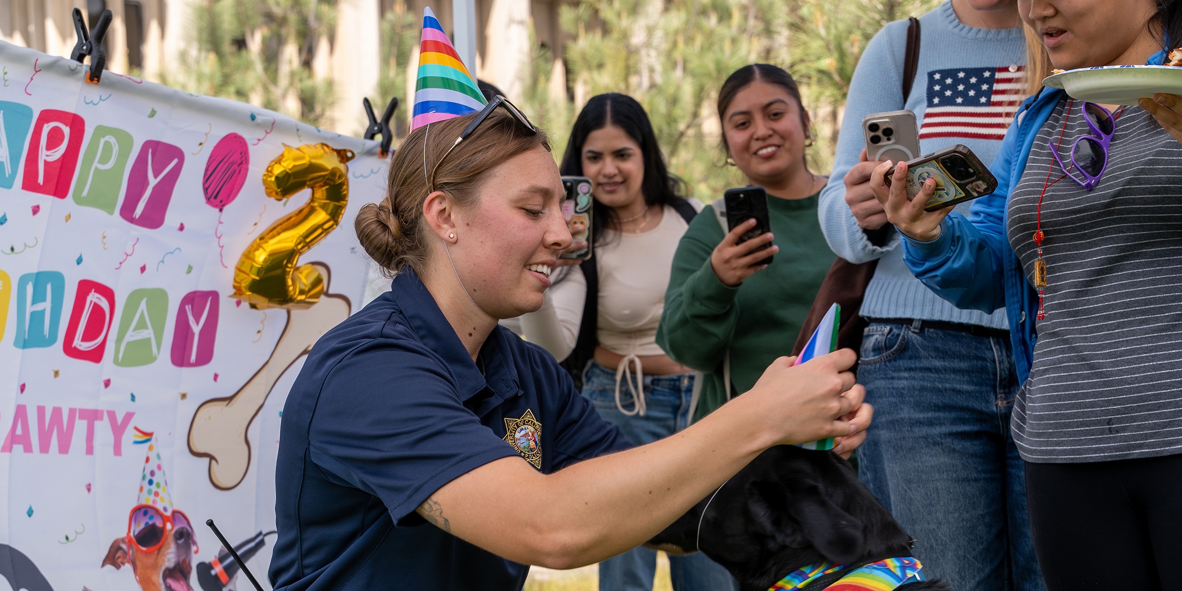 UC San Diego Police Officer Emma Dart places a paper party had on K-9 officer Diego for his birthday celebration. A crowd looked on and took photos. 