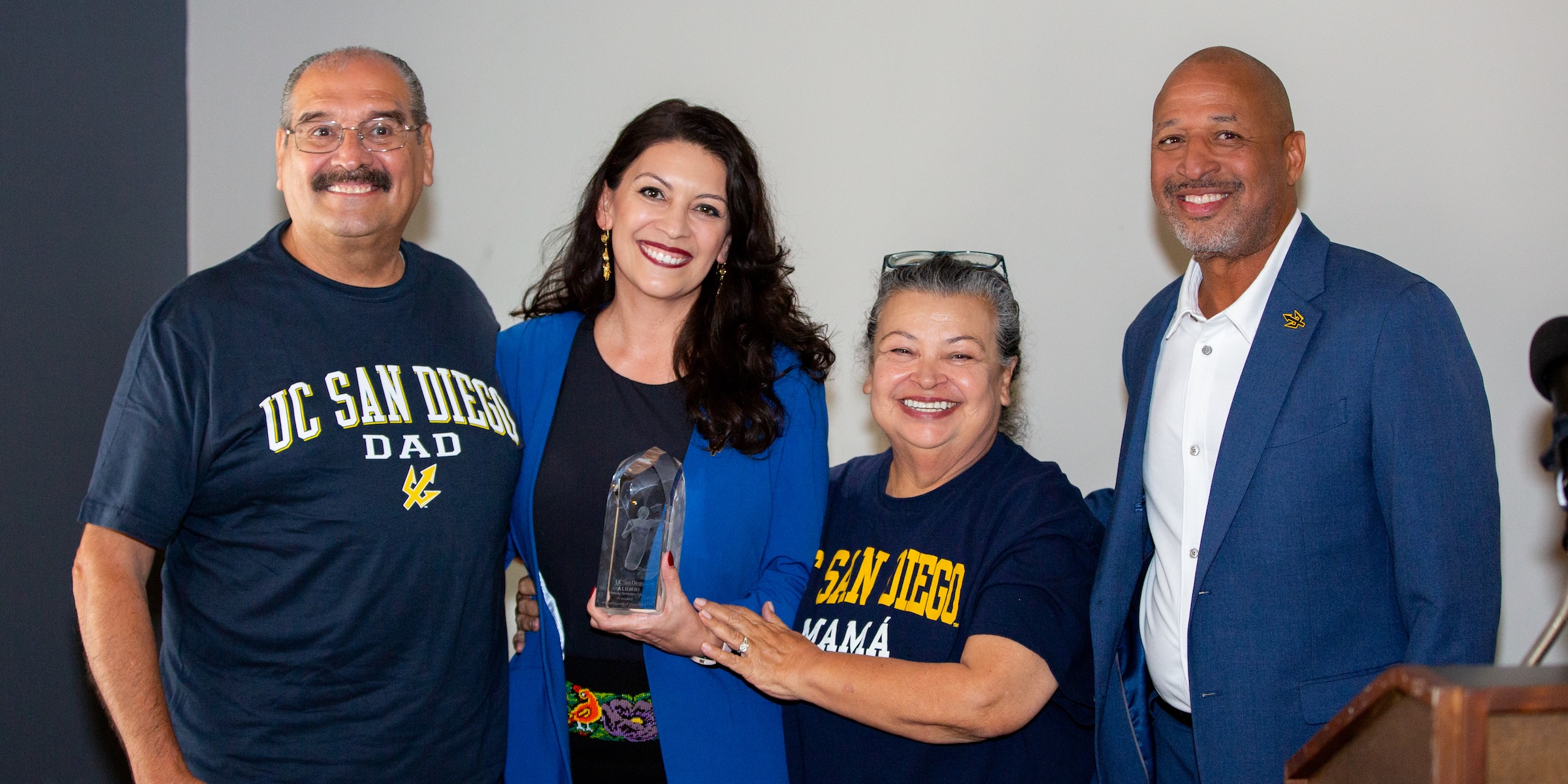 Four people smiling with one woman holding an award 