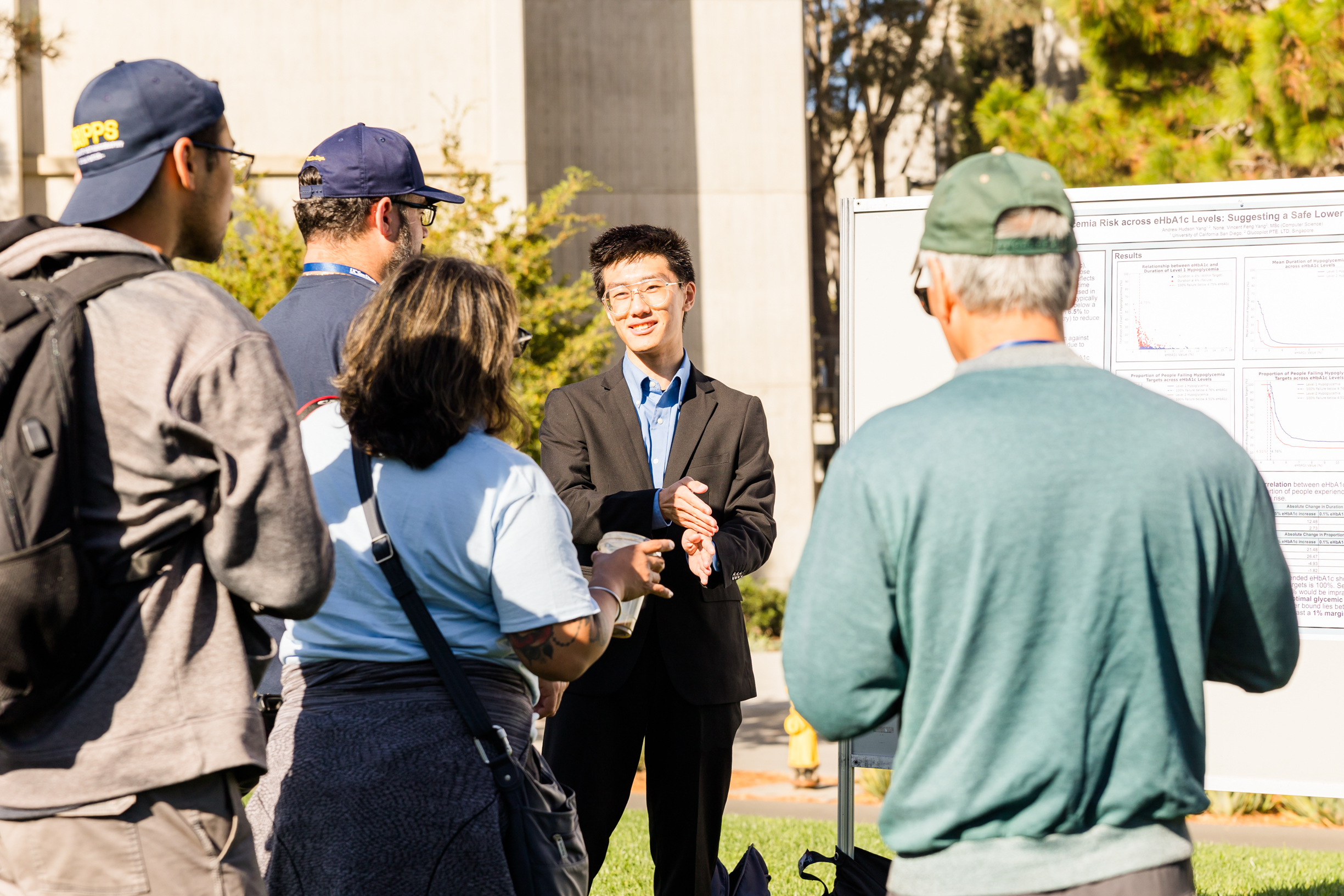 A student presents their research to a group in front of a whiteboard.