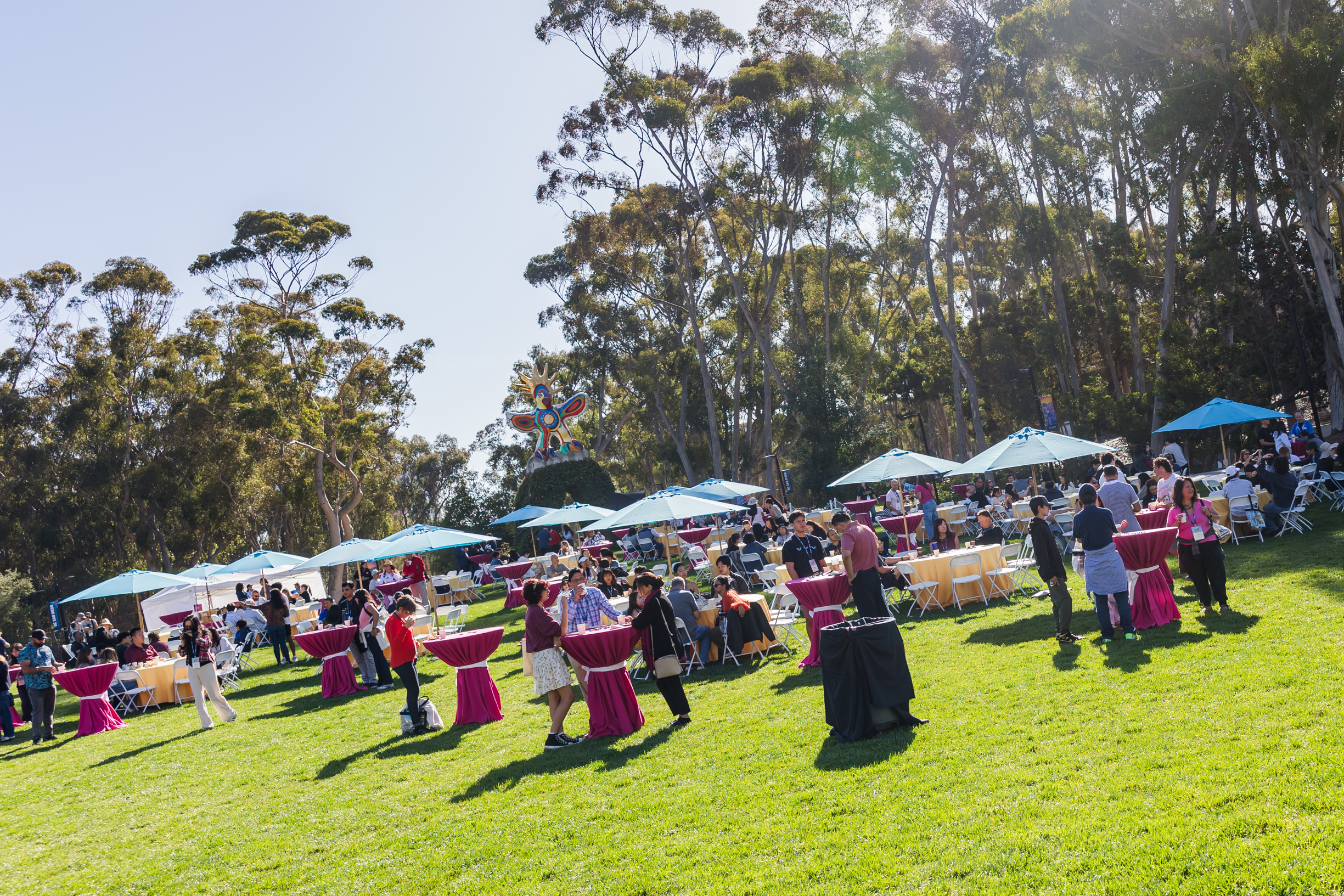Students and their families walk around Sun God Lawn with umbrellas and tables set up