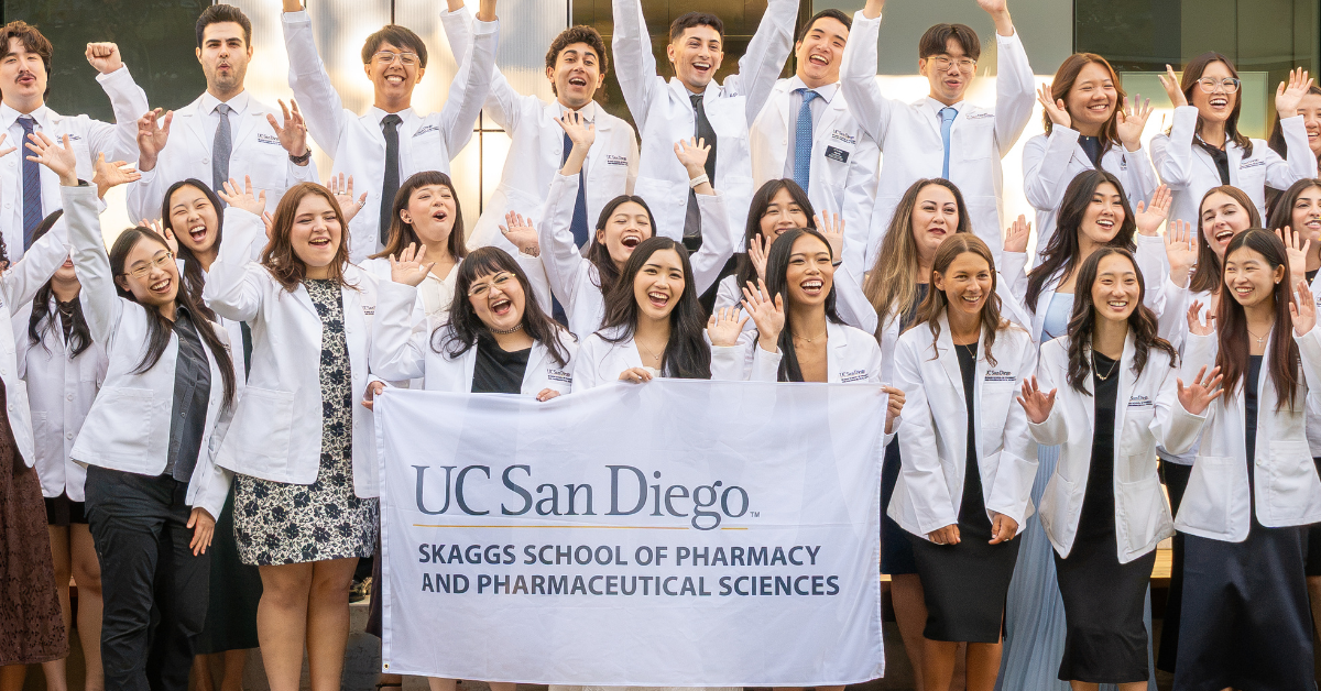 Pharmacy students in white coats holding a UC San Diego Skaggs School of Pharmacy and Pharmaceutical Sciences banner.